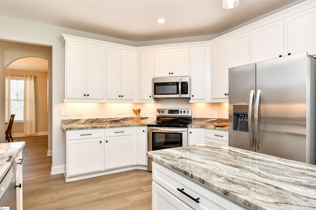 kitchen with white cabinets, appliances with stainless steel finishes, light stone countertops, and light hardwood / wood-style flooring