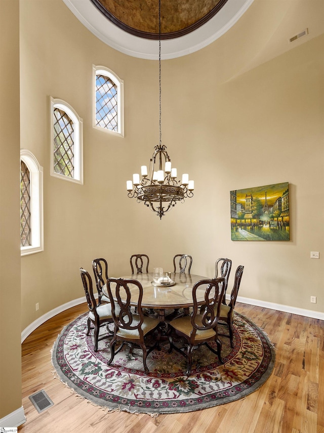 dining room with hardwood / wood-style floors, a towering ceiling, and ornamental molding