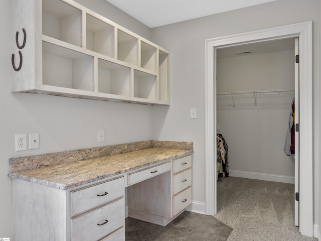 kitchen with dark carpet, light stone counters, and built in desk