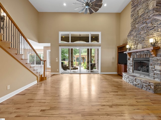 unfurnished living room with a stone fireplace, light hardwood / wood-style floors, and a high ceiling