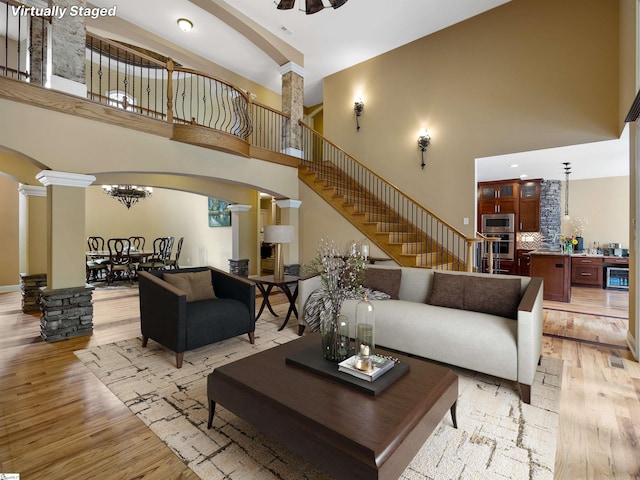 living room with ornate columns, ceiling fan, light hardwood / wood-style flooring, and a towering ceiling