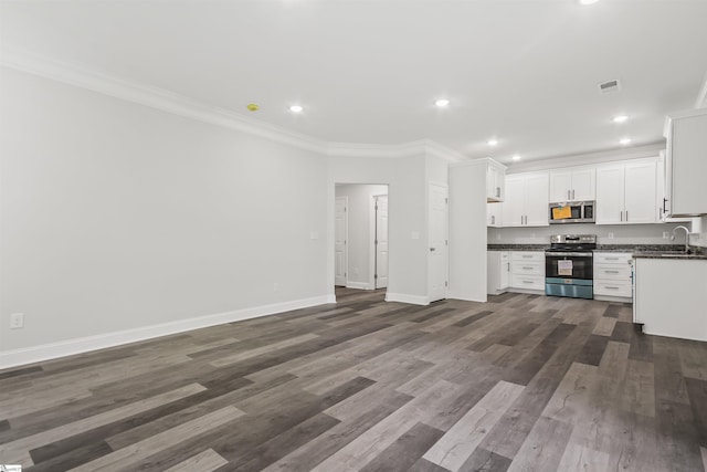 kitchen with dark wood-style flooring, ornamental molding, white cabinets, appliances with stainless steel finishes, and dark countertops