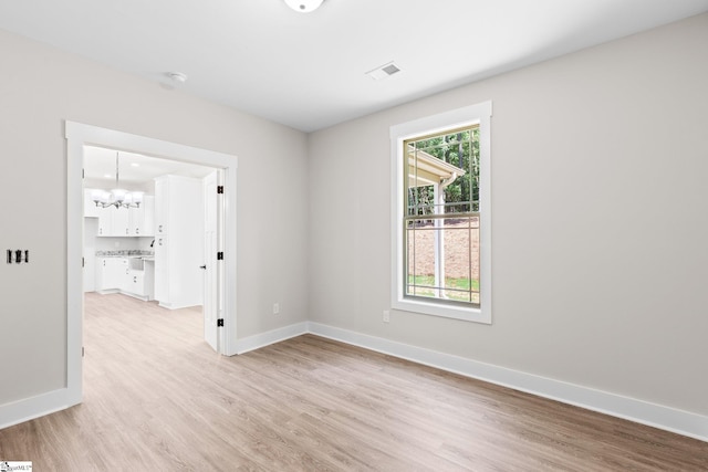 spare room with light wood-type flooring and an inviting chandelier