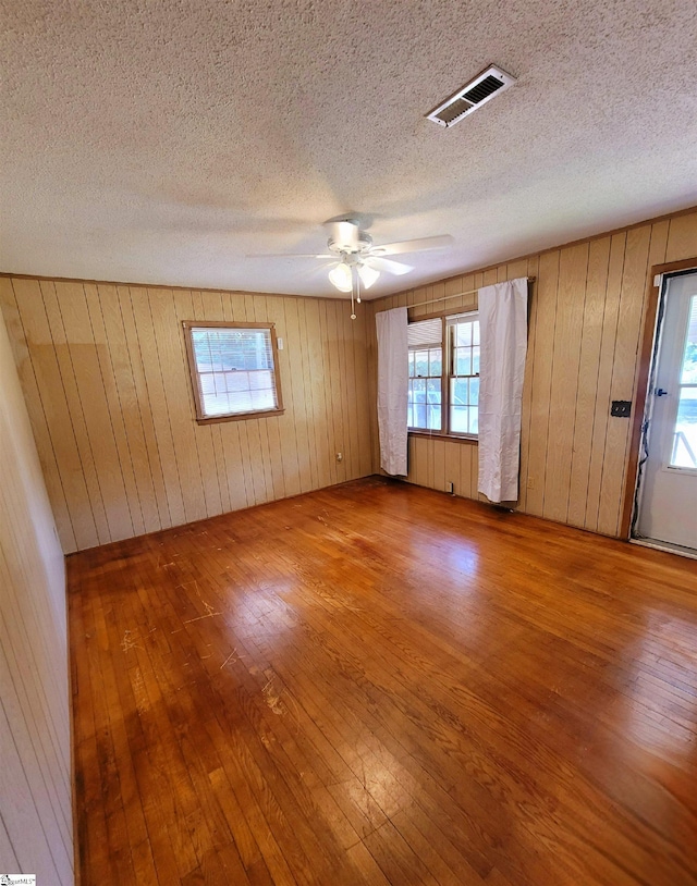 spare room featuring wooden walls, ceiling fan, wood-type flooring, and a textured ceiling