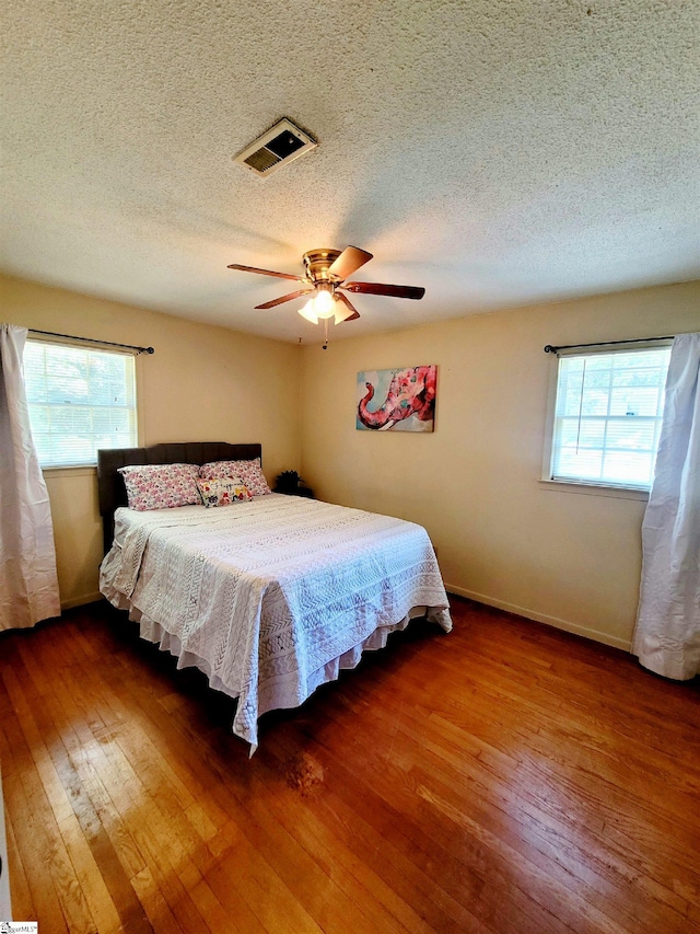 bedroom featuring multiple windows, ceiling fan, hardwood / wood-style floors, and a textured ceiling