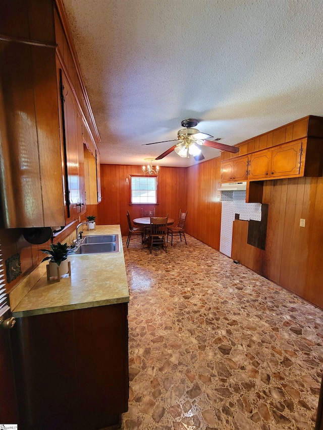 kitchen featuring wood walls, sink, ceiling fan, and a textured ceiling
