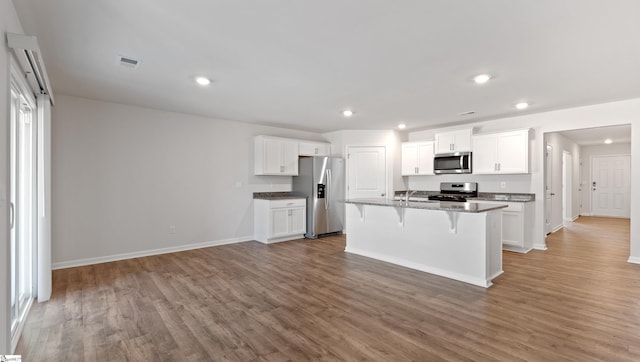 kitchen with an island with sink, white cabinetry, a kitchen bar, hardwood / wood-style flooring, and stainless steel appliances