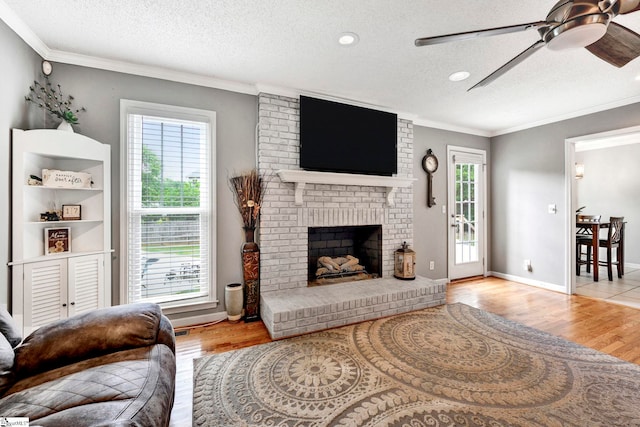 living room with light hardwood / wood-style floors, crown molding, a textured ceiling, and a brick fireplace