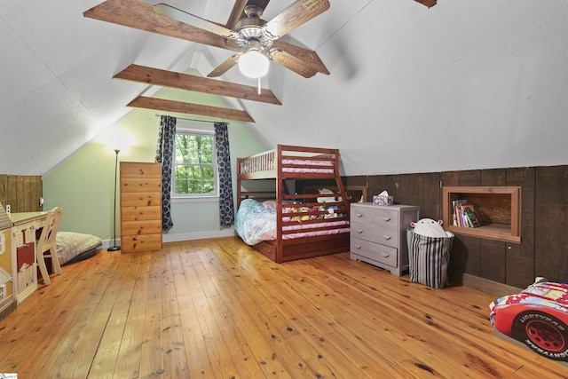 bedroom with ceiling fan, wooden walls, light hardwood / wood-style floors, and lofted ceiling