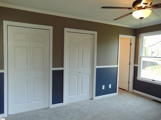 unfurnished bedroom with multiple closets, ceiling fan, crown molding, and light colored carpet