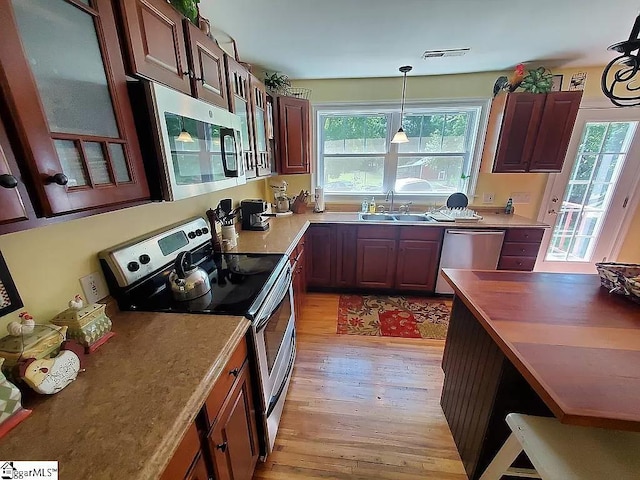 kitchen featuring sink, light hardwood / wood-style flooring, hanging light fixtures, and appliances with stainless steel finishes