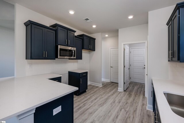 kitchen with light wood finished floors, tasteful backsplash, light countertops, stainless steel microwave, and visible vents