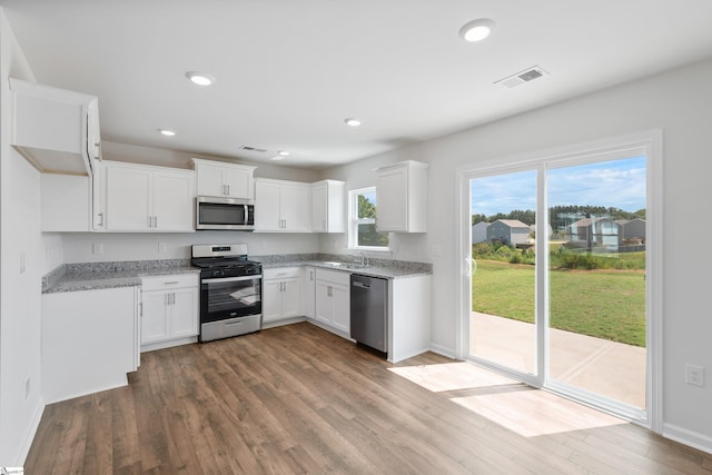 kitchen with sink, light stone counters, appliances with stainless steel finishes, white cabinets, and hardwood / wood-style flooring