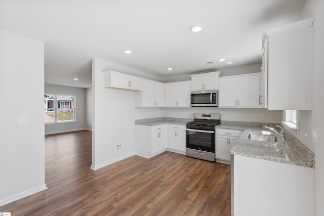 kitchen with appliances with stainless steel finishes, dark hardwood / wood-style flooring, light stone counters, sink, and white cabinets