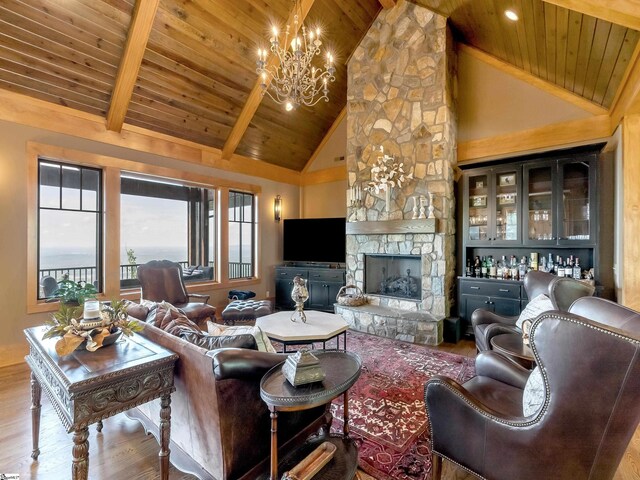 living room with beam ceiling, wooden ceiling, a stone fireplace, high vaulted ceiling, and a chandelier