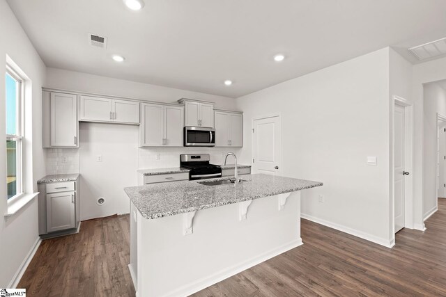 kitchen with sink, light stone counters, dark hardwood / wood-style floors, a center island with sink, and appliances with stainless steel finishes