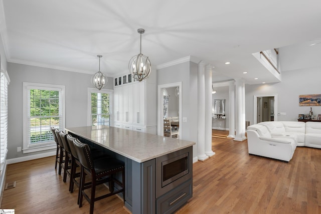 kitchen with stainless steel microwave, decorative light fixtures, decorative columns, light hardwood / wood-style floors, and light stone counters