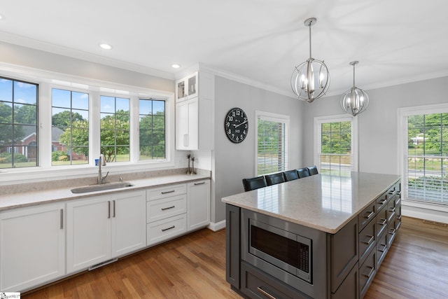 kitchen featuring pendant lighting, sink, white cabinetry, stainless steel microwave, and light wood-type flooring