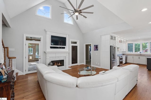 living room featuring ceiling fan, wood-type flooring, a premium fireplace, and high vaulted ceiling