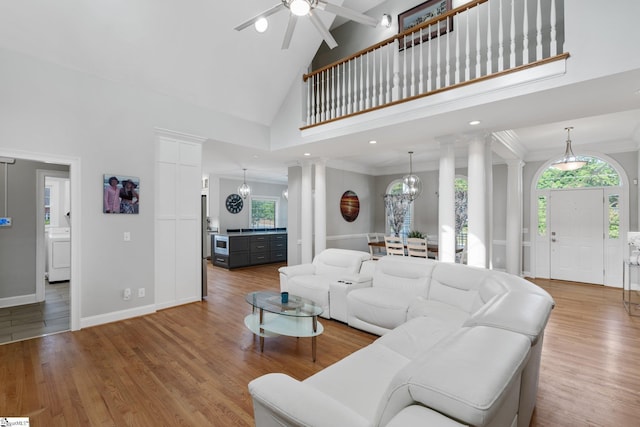 living room featuring hardwood / wood-style floors, high vaulted ceiling, decorative columns, washer / dryer, and crown molding