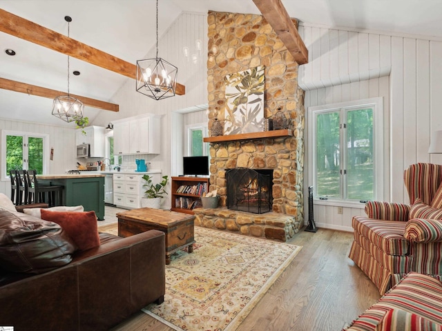 living area with high vaulted ceiling, light wood-style floors, a stone fireplace, a chandelier, and beamed ceiling