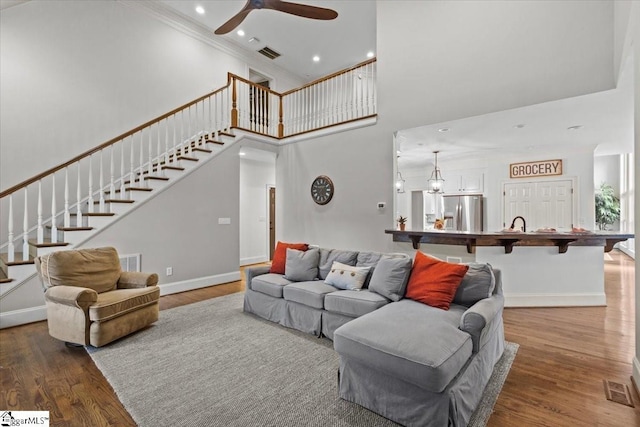 living room featuring hardwood / wood-style flooring, ceiling fan, a towering ceiling, and crown molding