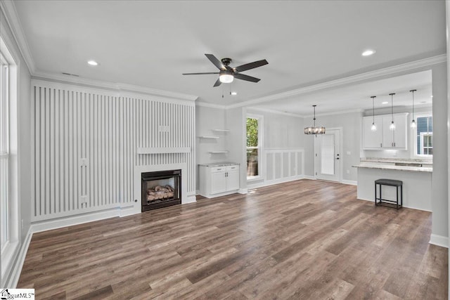 unfurnished living room with crown molding, a large fireplace, ceiling fan with notable chandelier, and hardwood / wood-style flooring