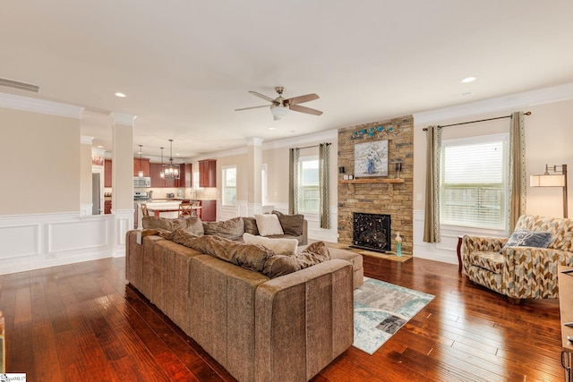 living room with ceiling fan with notable chandelier, dark hardwood / wood-style floors, a stone fireplace, and a healthy amount of sunlight