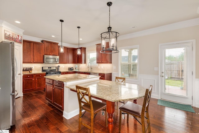 kitchen with pendant lighting, a center island, ornamental molding, appliances with stainless steel finishes, and dark hardwood / wood-style flooring