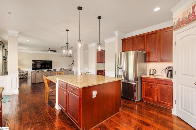 kitchen with light stone countertops, stainless steel fridge, ceiling fan with notable chandelier, a center island, and hanging light fixtures