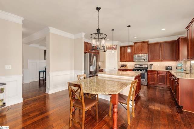 kitchen with sink, stainless steel appliances, light stone counters, decorative light fixtures, and a kitchen island