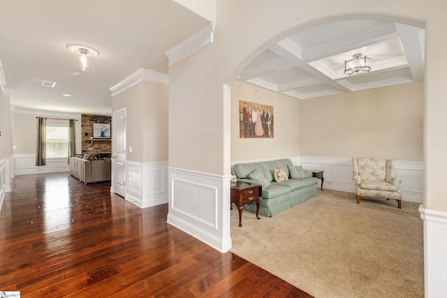 carpeted living room with beam ceiling, a stone fireplace, coffered ceiling, and ornamental molding