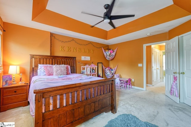 bedroom with a tray ceiling, ceiling fan, and light carpet