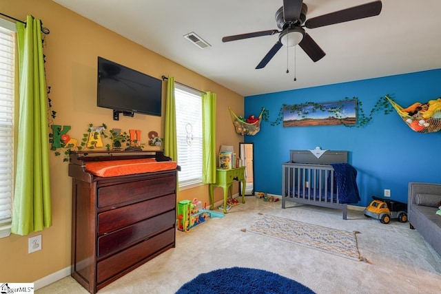 bedroom featuring ceiling fan, light carpet, and a nursery area