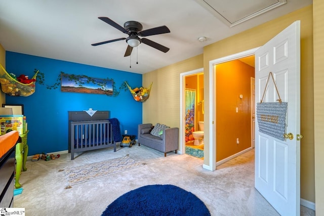 bedroom featuring carpet, a nursery area, ceiling fan, and ensuite bath