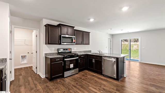 kitchen with dark brown cabinetry, sink, dark wood-type flooring, kitchen peninsula, and appliances with stainless steel finishes