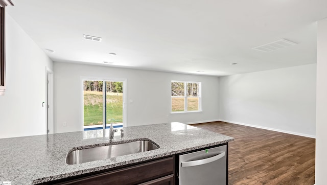 kitchen with stainless steel dishwasher, light stone counters, dark brown cabinetry, and sink