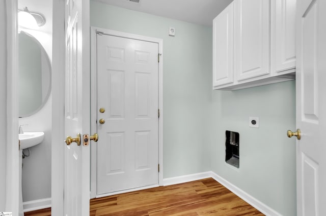 washroom with electric dryer hookup, cabinets, and light hardwood / wood-style floors