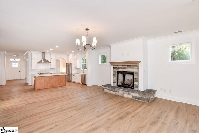 unfurnished living room with sink, ornamental molding, a fireplace, a notable chandelier, and light hardwood / wood-style floors