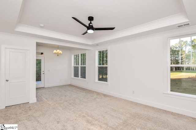 empty room featuring a tray ceiling, light carpet, crown molding, and ceiling fan with notable chandelier