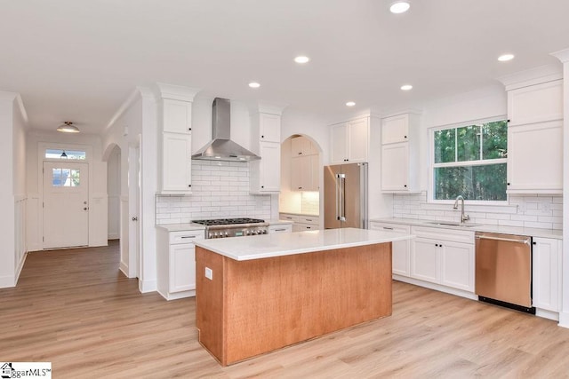 kitchen featuring a center island, white cabinets, sink, wall chimney exhaust hood, and appliances with stainless steel finishes