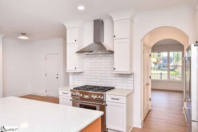 kitchen featuring backsplash, white cabinets, stainless steel appliances, and wall chimney range hood