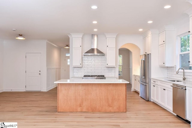 kitchen featuring white cabinetry, a center island, sink, stainless steel appliances, and wall chimney range hood