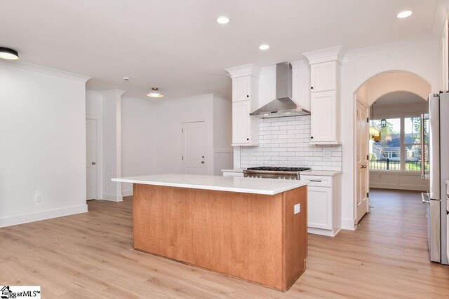 kitchen with white cabinetry, a center island, wall chimney exhaust hood, and ornamental molding