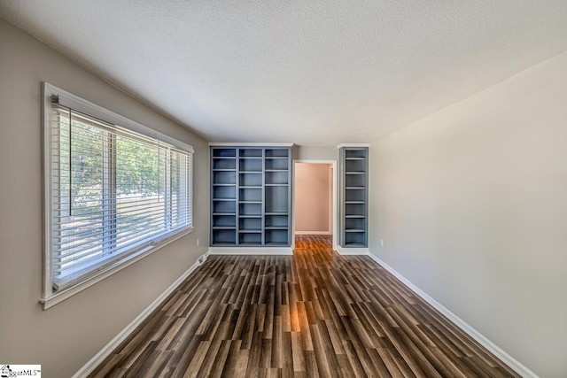 spare room with built in shelves, dark hardwood / wood-style floors, and a textured ceiling