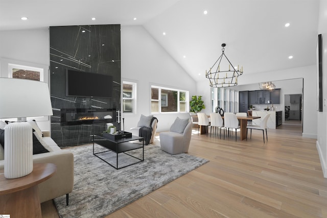 living room featuring high vaulted ceiling, light hardwood / wood-style floors, a tile fireplace, and a notable chandelier