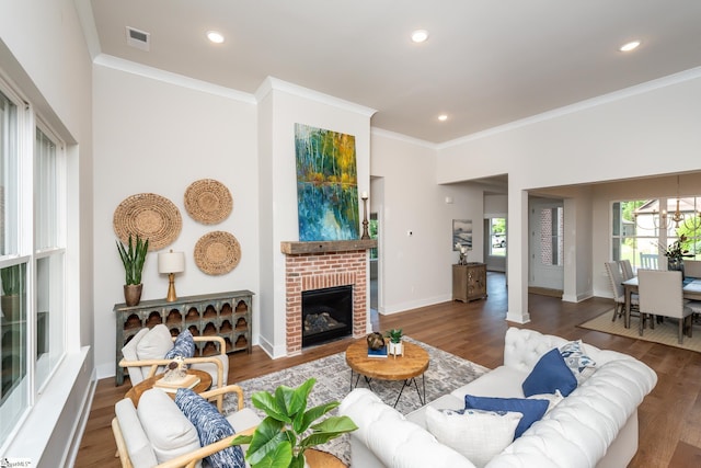 living room with crown molding, a notable chandelier, dark hardwood / wood-style floors, and a brick fireplace