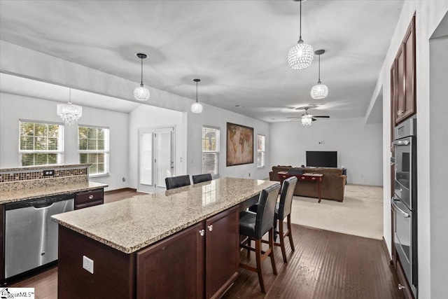 kitchen with pendant lighting, a center island, ceiling fan with notable chandelier, stainless steel dishwasher, and a breakfast bar area