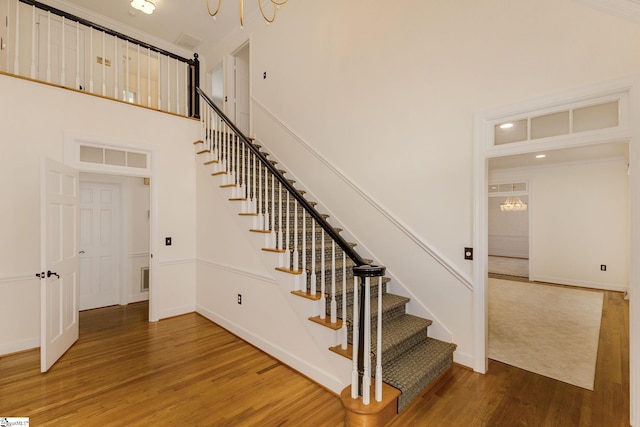 stairway with wood-type flooring, an inviting chandelier, crown molding, and a high ceiling