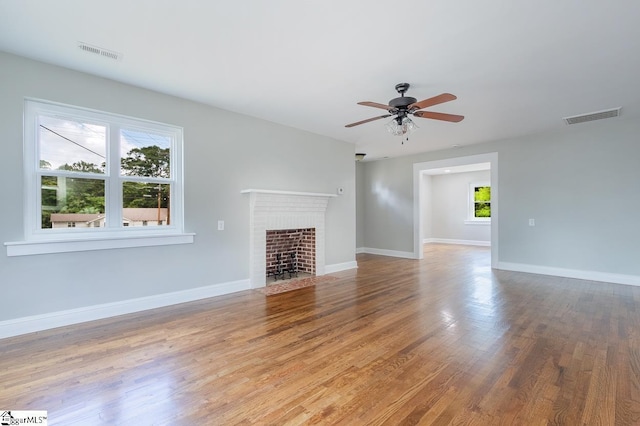 unfurnished living room with hardwood / wood-style flooring, a brick fireplace, plenty of natural light, and ceiling fan